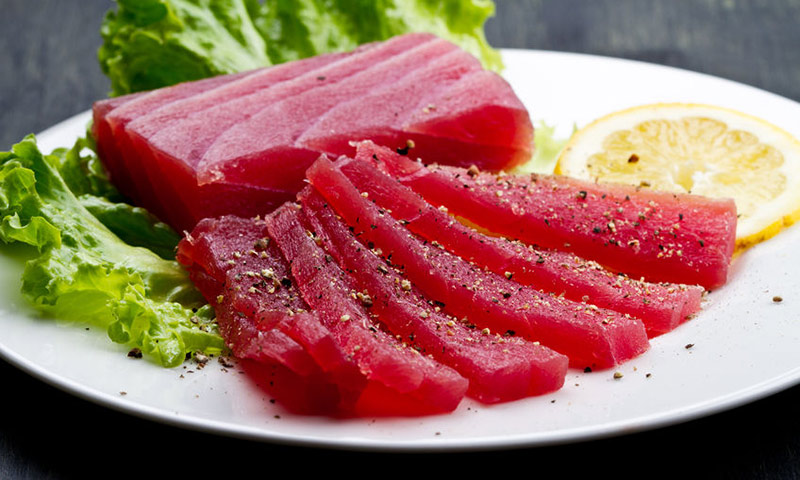 Filés de atum cru, rosados e temperados, sobre um prato com rodela de laranja e folha de alface.