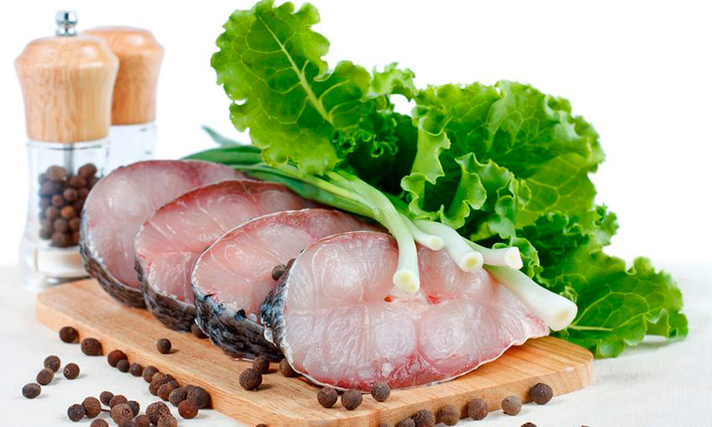 Postas de linguado sobre uma tábua de madeira, com folhas de alface e pimenta-do-reino preta.