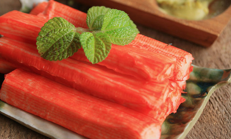 Porção de kani kama com folha de hortelã, sobre uma peça de louça japonesa.